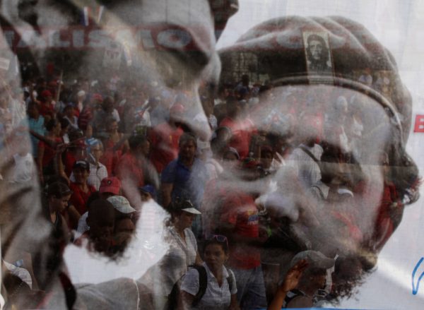 People are seen through a poster with a picture of Cuba's former leader Fidel Castro and late Argentine revolution leader Che Guevara (L) during the May Day parade in Havana's Revolution Square in this May 1, 2013 file photo. REUTERS/Desmond Boylan/File Photo